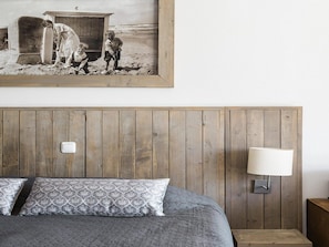 A bedroom with a wooden headboard, a bed with patterned pillows, a nightstand, and a wall-mounted lamp. - Seaside Double Duyn Suites (Callantsoog)