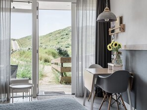Ein Zimmer mit Schreibtisch, Stuhl und Blick auf eine grüne Landschaft durch eine Glastür.