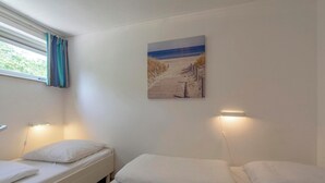 Ein Zimmer mit zwei Einzelbetten, einem mit Vorhängen versehenen Fenster, einem an der Wand hängenden Strandbild und einer Wandleuchte.