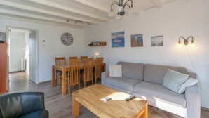 Ein Wohnzimmer mit einem Holzesstisch, einer Couch und einem Couchtisch. An der Wand hängt eine Uhr und es gibt eine Chandelüstere.