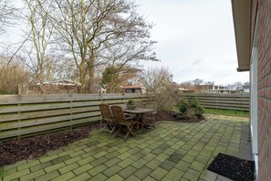 Une terrasse avec une table et des chaises, entourée d’un mur de briques et d’une clôture en bois.