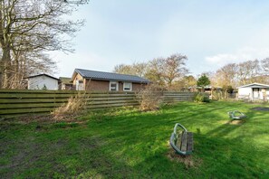 Une cour arrière verdoyante, avec une clôture en bois, une balançoire et une maison dont le toit est recouvert de tuiles.