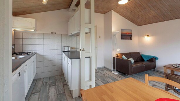 Une cuisine compacte avec des meubles blancs, une cuisinière et un coin repas comprenant une table et des chaises en bois.