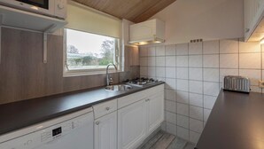 Une cuisine avec des meubles blancs, un lave-vaisselle Bosch, un four à micro-ondes, une cuisinière à gaz et un grille-pain.
