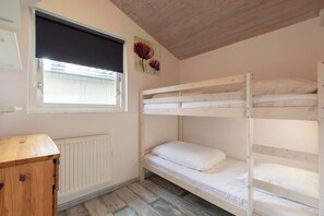 Une chambre avec un lit superposé, une tête de lit en bois, un radiateur, une fenêtre avec un store noir et une armoire en bois.