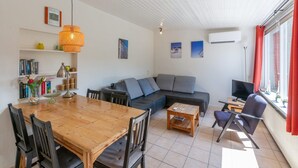 Un salon moderne avec une table à manger en bois, un canapé gris et un téléviseur. On y trouve également des étagères et un rideau rouge à la fenêtre.