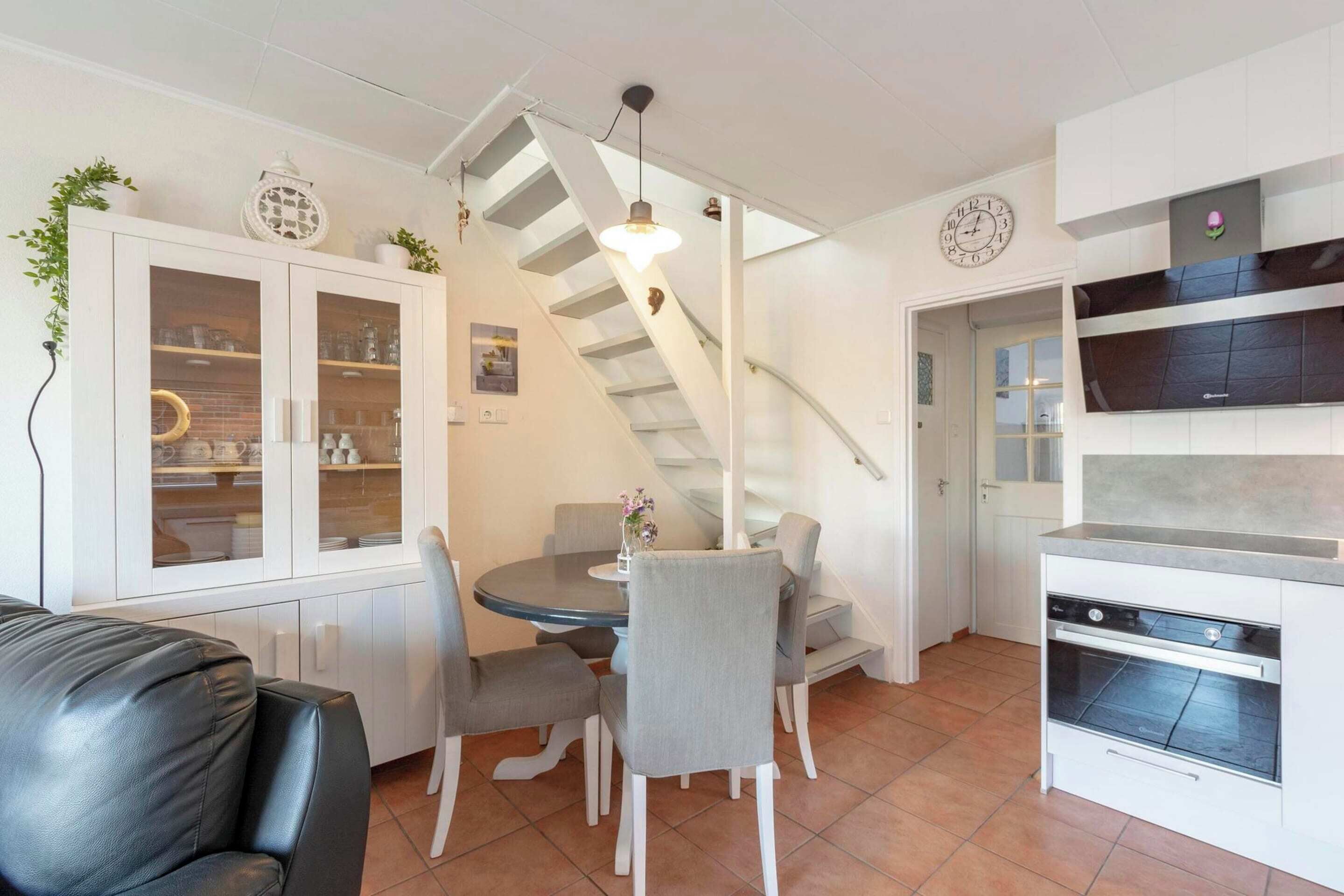 Una cocina moderna con comedor, muebles de cocina blancos, horno empotrado y una escalera.
