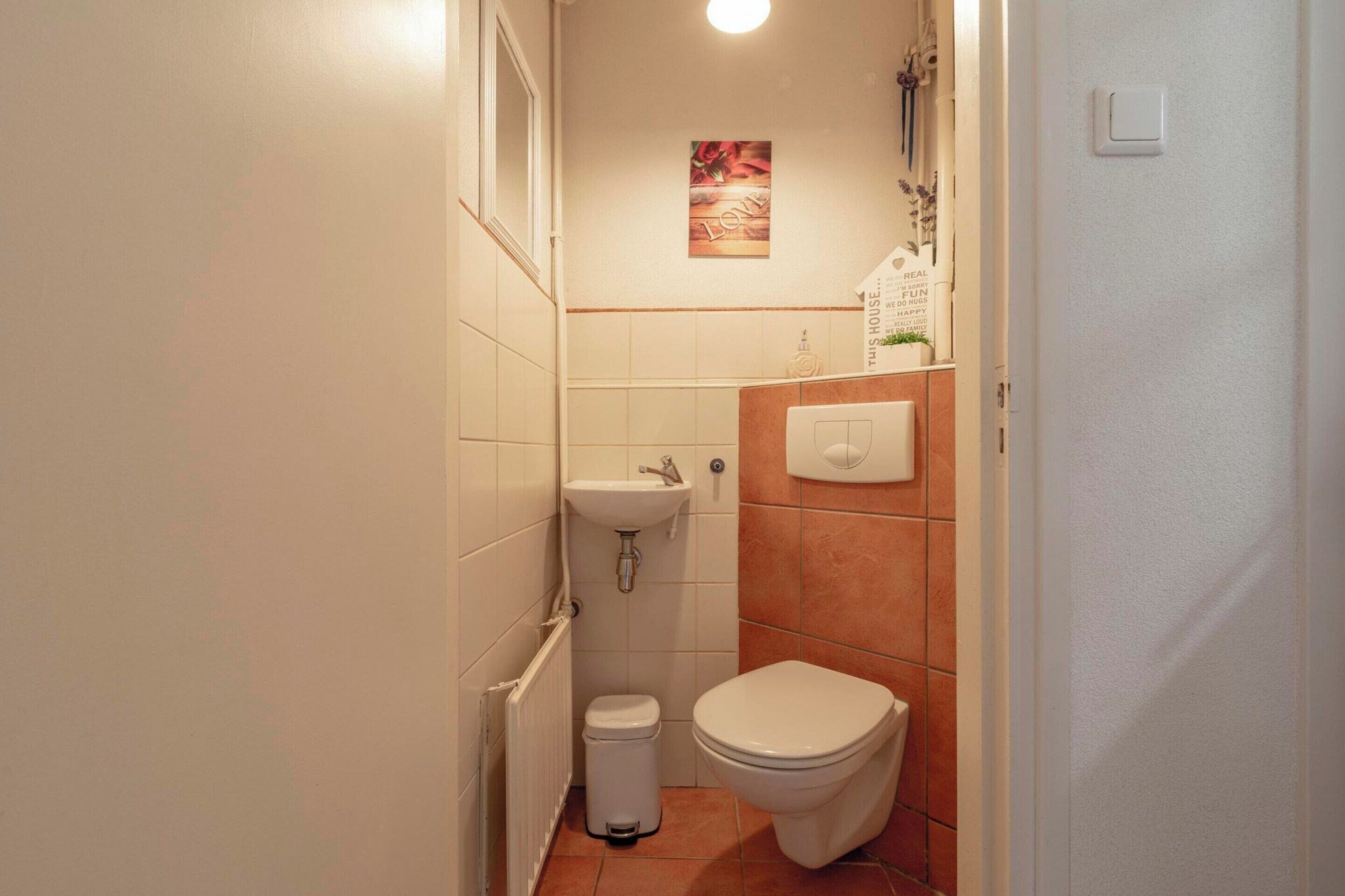 A small, compact bathroom with a white sink, toilet, and trash bin.