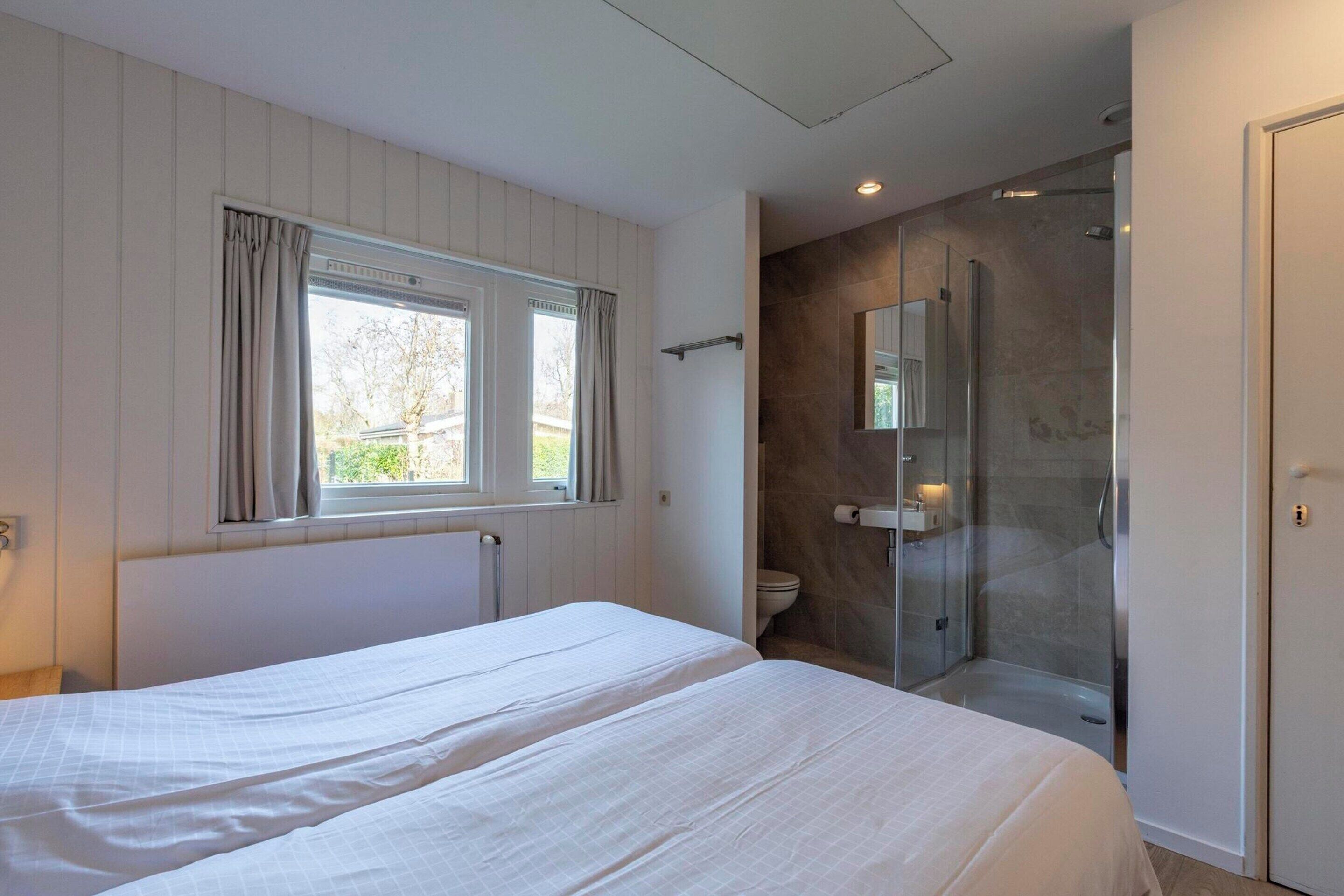 A modern hotel room with two beds, a shower area, and a large window.