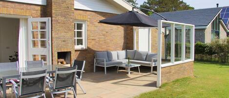 An outdoor patio with a brick fireplace, a glass-enclosed seating area, and a table with chairs.