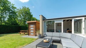 Una zona relax moderna all'aperto con tavolo e divano, una panca in legno e una porta vetrata che dà su un patio.