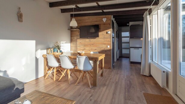 Una cucina moderna con travi in legno, un'area pranzo con tavolo e sedie in legno, e un'ampia finestra che permette alla luce naturale di illuminare l'ambiente.