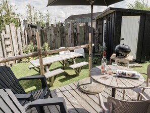 A patio area with wooden tables and chairs, a barbecue grill, and a bottle of wine. - Family Beach Getaway (Callantsoog)