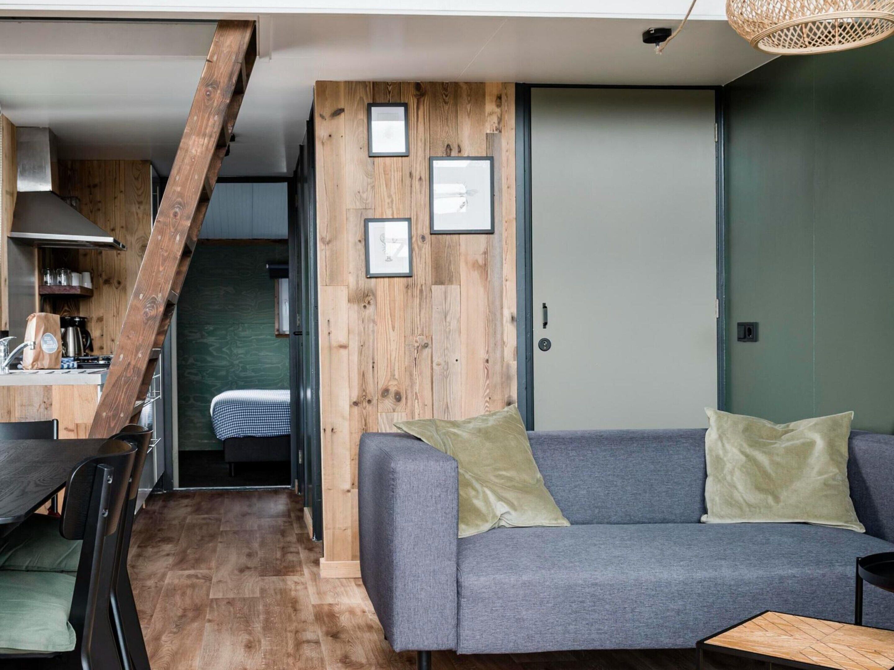 A modern living space with a grey sofa, wooden accents, and a staircase leading to a kitchen area.