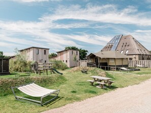 A campsite with wooden cabins, a picnic table, a hammock, and a play structure. - Family Beach Getaway (Callantsoog)