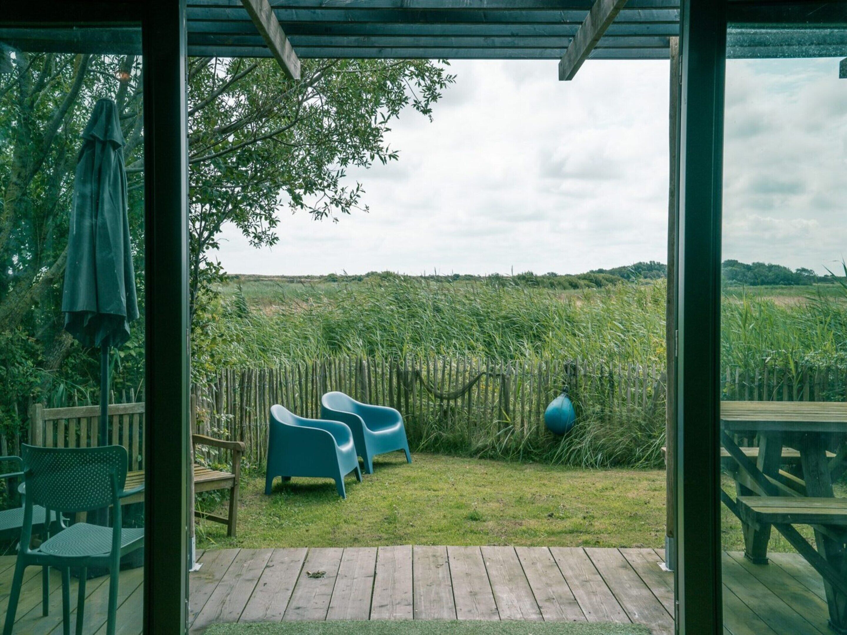 Un espace extérieur aménagé en terrasse, avec une plateforme en bois, deux chaises bleues et une table en bois.