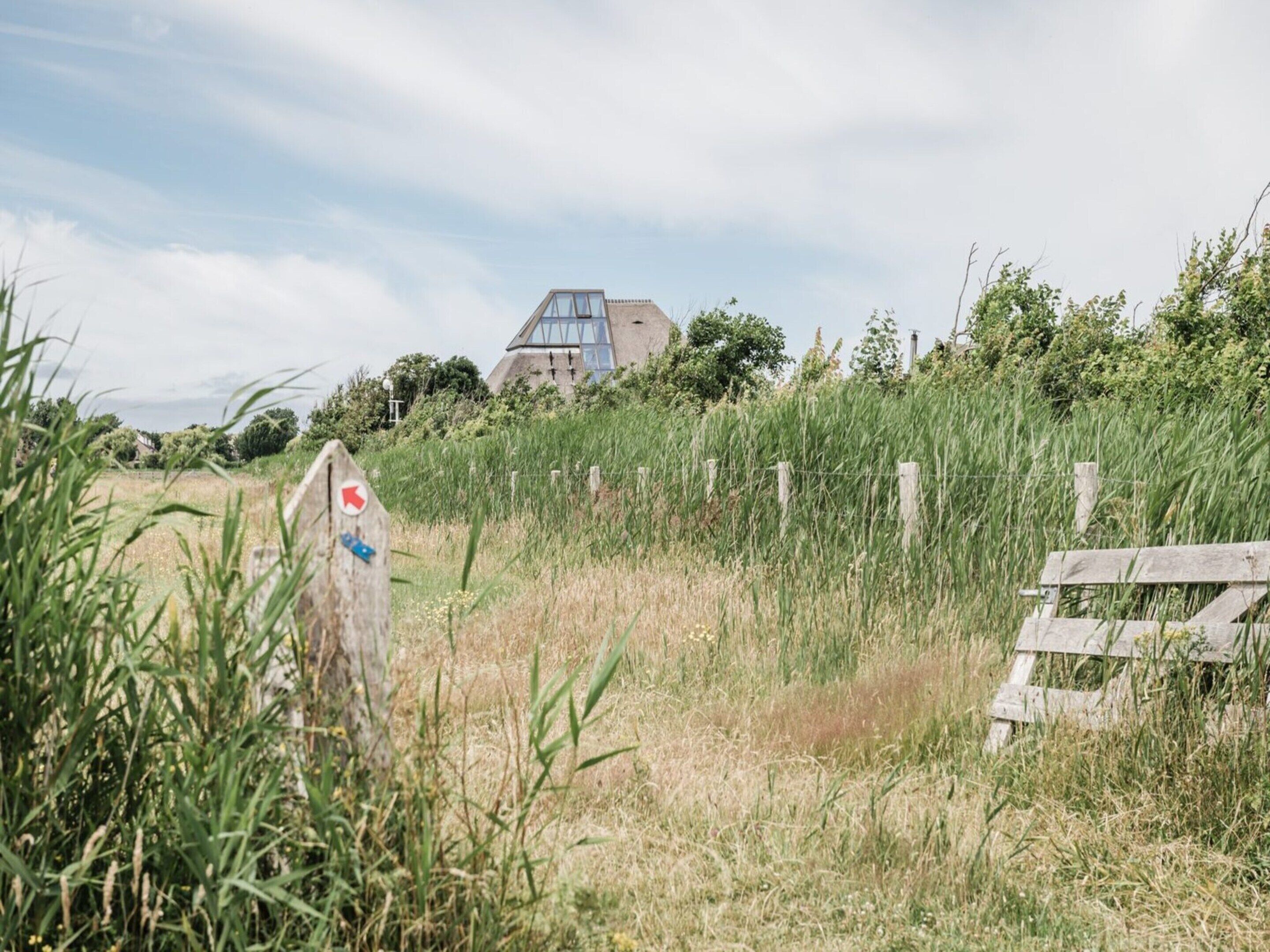 A rural landscape with a house featuring a large glass window and a triangular roof.