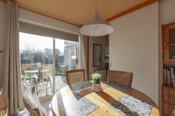 Enjoy meals in this cozy dining area with a round table and four chairs, surrounded by a potted plant and a sliding glass door leading to an outdoor patio.
