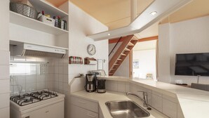 A modern kitchen with a gas stove, stainless steel sink, and a built-in oven. There is a clock on the wall and a television mounted above the counter. - Cozy Holiday Home With Terrace (Callantsoog)