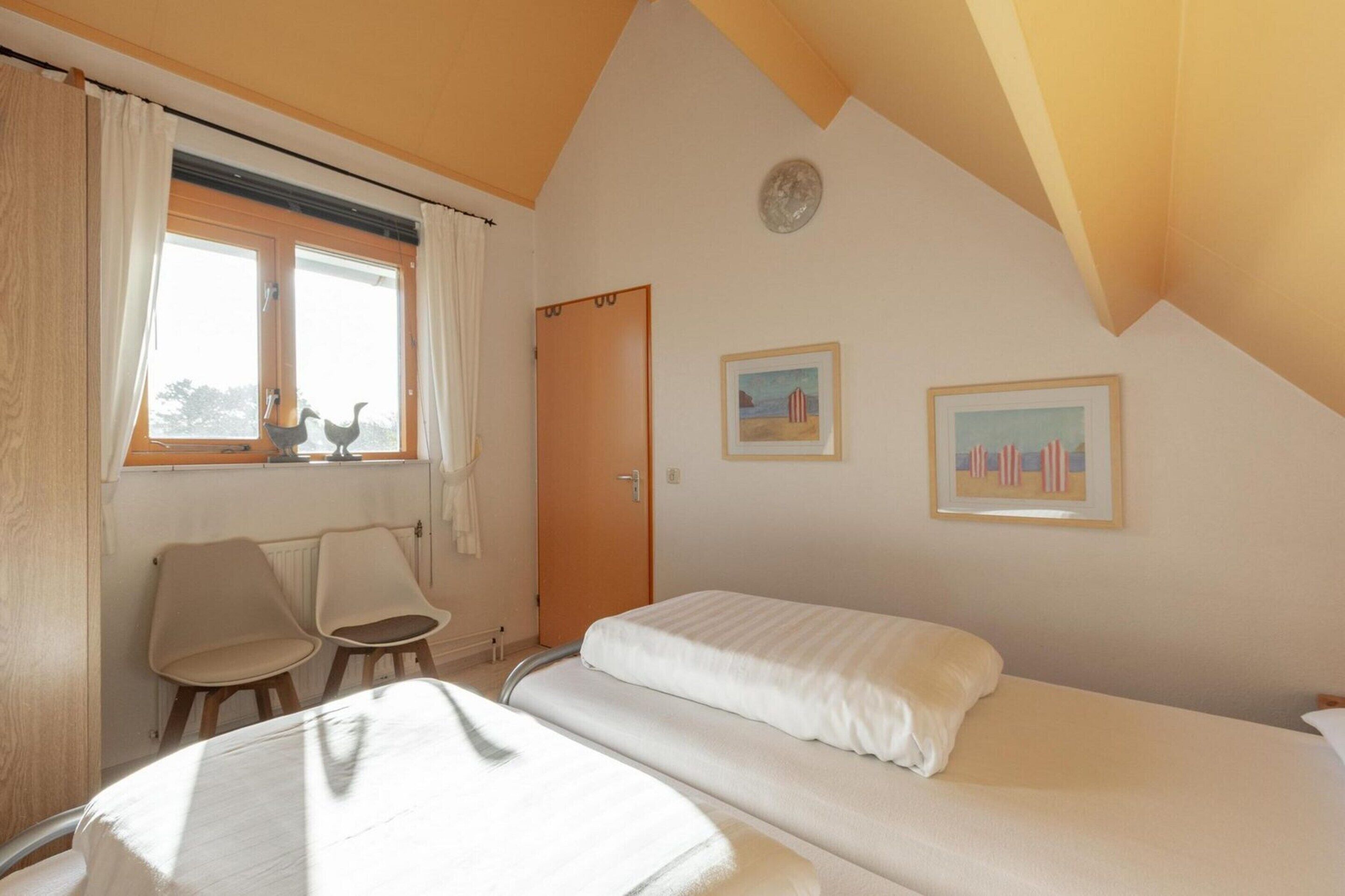 Une chambre avec deux lits, une fenêtre avec des rideaux, une porte et deux tableaux encadrés accrochés au mur.