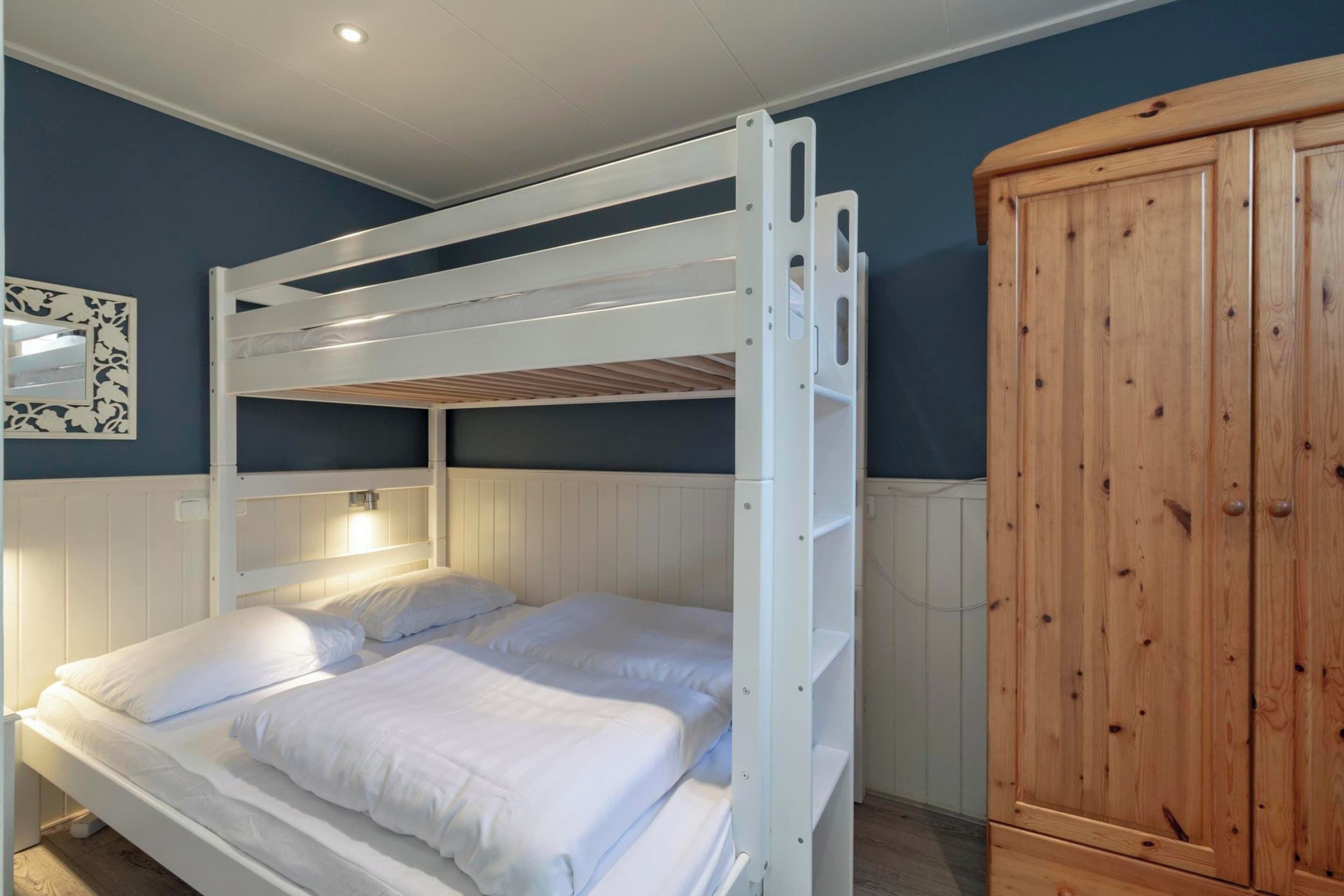 A bunk bed with white bedding and a wooden wardrobe.