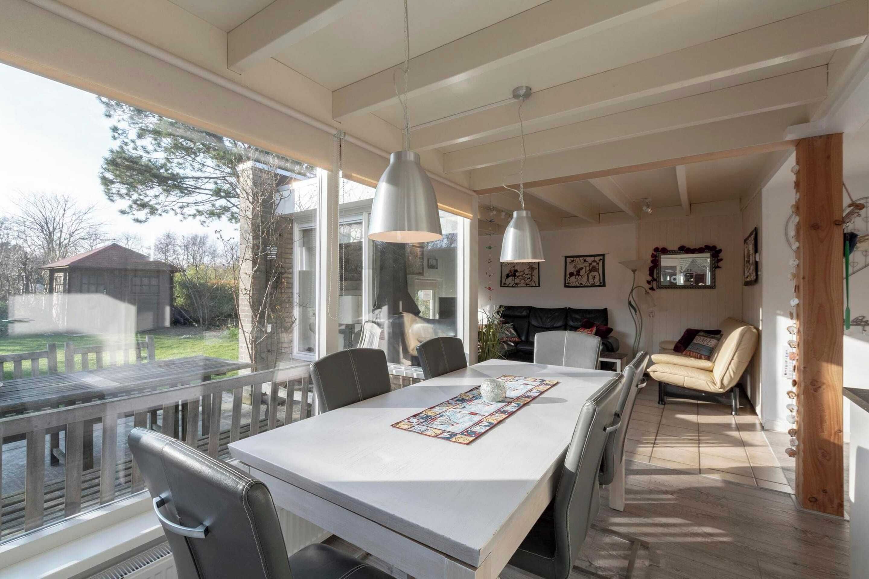 A dining area with a large table, chairs, pendant lights, and a view of the outdoors.