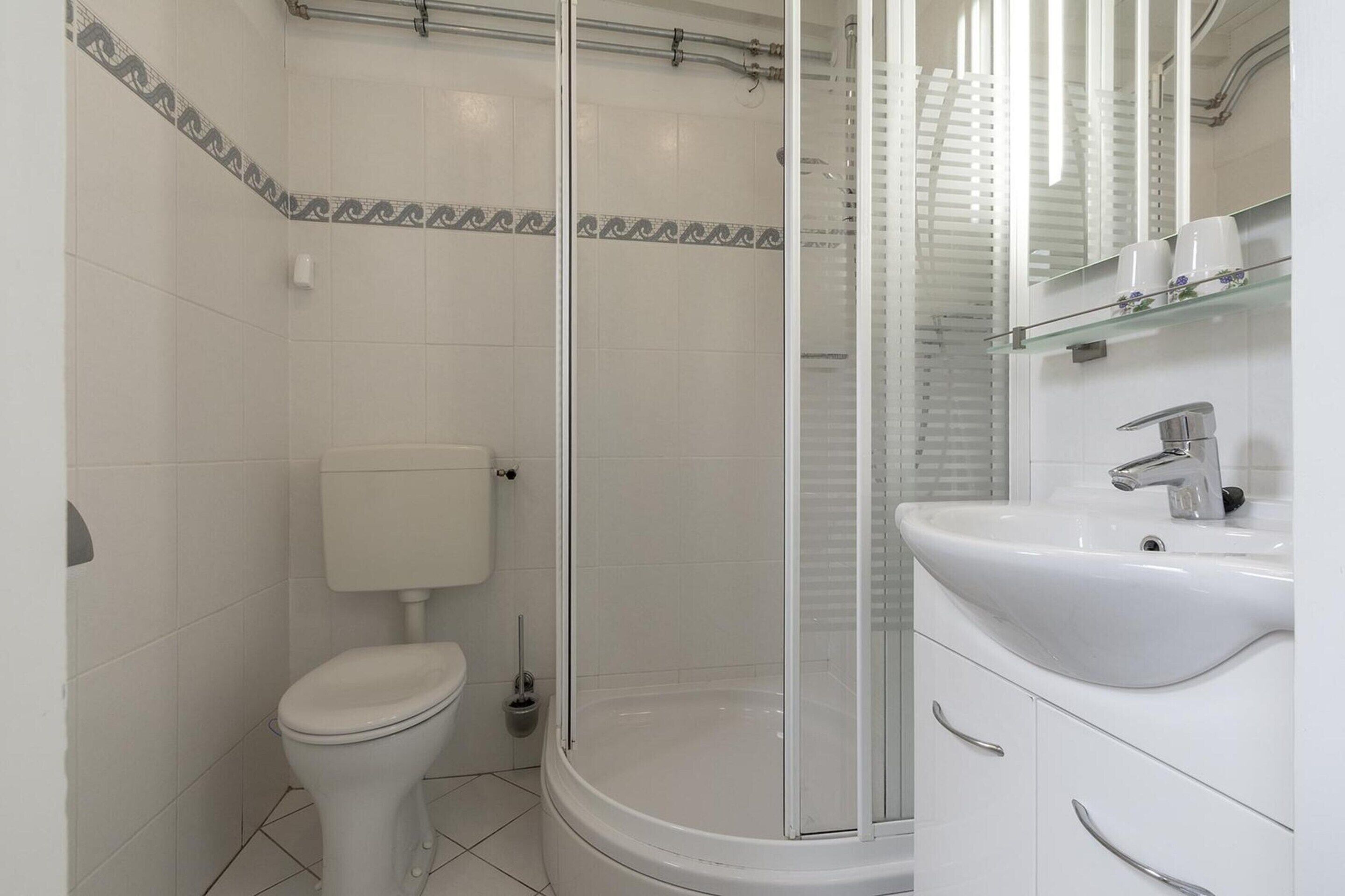 A modern bathroom with a toilet, shower enclosure, and a sink with a mirror.
