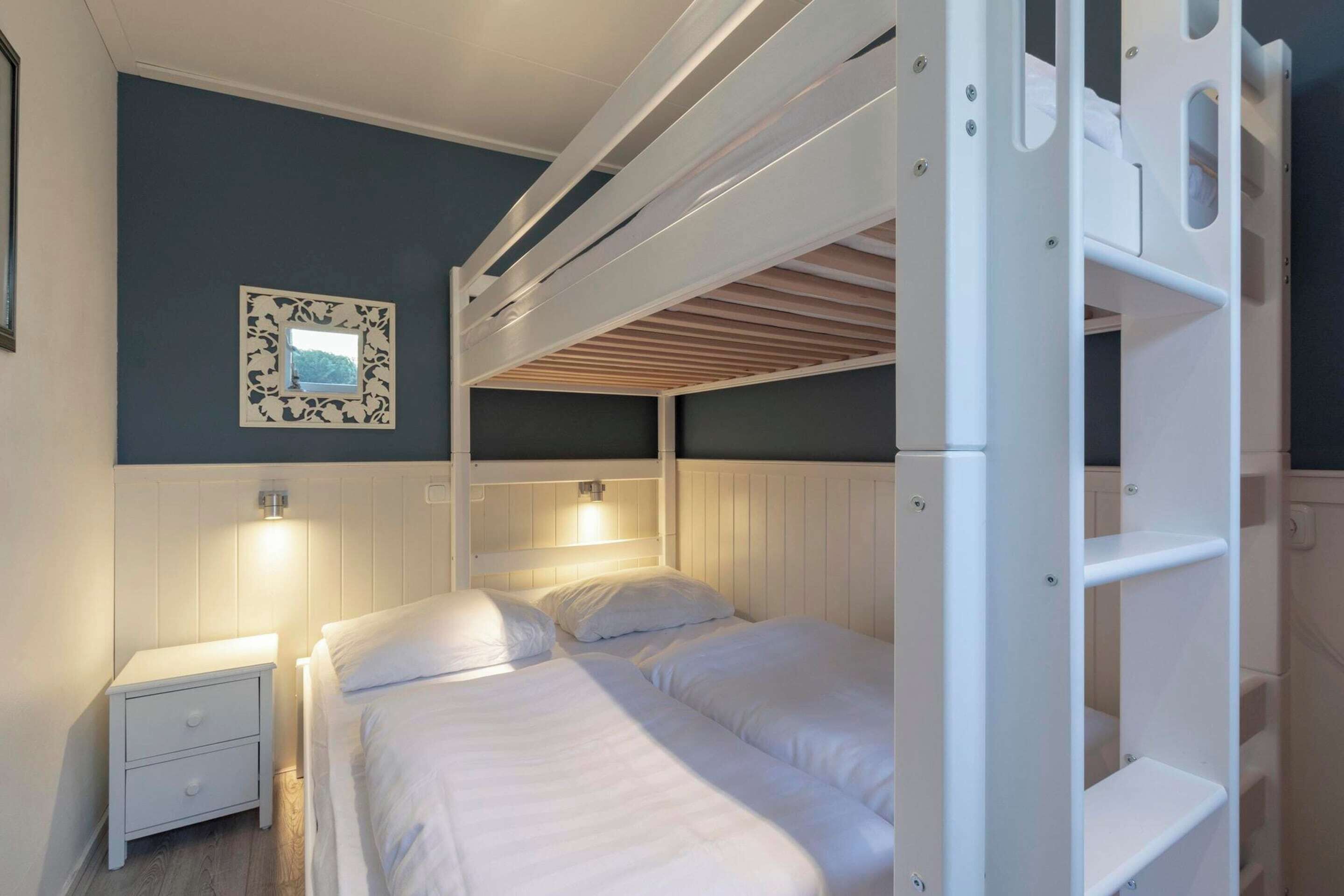 A bunk bed room with a nightstand, a framed picture on the wall, and a white headboard.