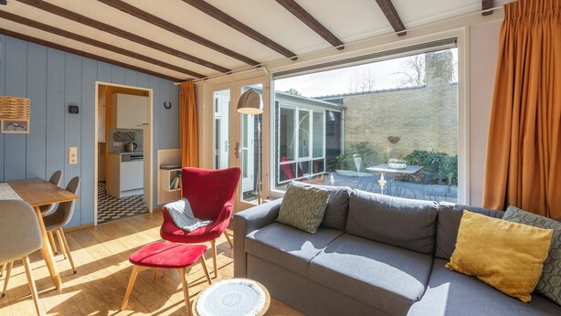 A cozy living room with a sofa, red chair, and a dining table. - Bungalow in Sint Maartenszee Near Dunes (Sint Maartensvlotbrug)