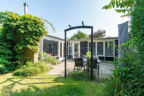 Un espace patio aménagé avec une table et des chaises, entouré de verdure et doté d’une structure couverte.