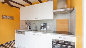 A kitchen with white cabinets, a dishwasher, a coffee maker, and an oven. - Bungalow in Sint Maartenszee Near Dunes (Sint Maartensvlotbrug)