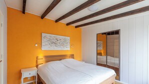 A bedroom with a wooden bed, white nightstand, and a painting on the wall. - Bungalow in Sint Maartenszee Near Dunes (Sint Maartensvlotbrug)