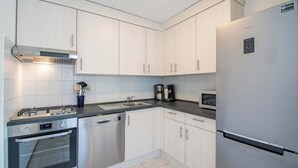 Eine moderne Küche mit weißen Schränken, Edelstahlgeräten, darunter ein Geschirrspüler, ein Backofen und ein Kühlschrank, eine Mikrowelle und eine Kaffeemaschine.