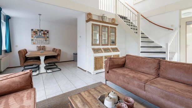 Ein geräumiges Wohnzimmer mit einer braunen Ledersofa, einem Holztisch und einem Essbereich mit einem weißen Schrank sowie einer Treppe.