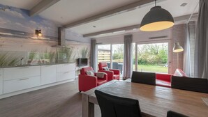 A modern dining area with a wooden table and red upholstered chairs, a large pendant light, and a view of the outdoors through a glass door. - Holiday Home on Car-free Park Garnekuul (Callantsoog)