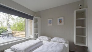 A bedroom with two beds, a window with a view of a patio, and built-in shelving. - Holiday Home on Car-free Park Garnekuul (Callantsoog)