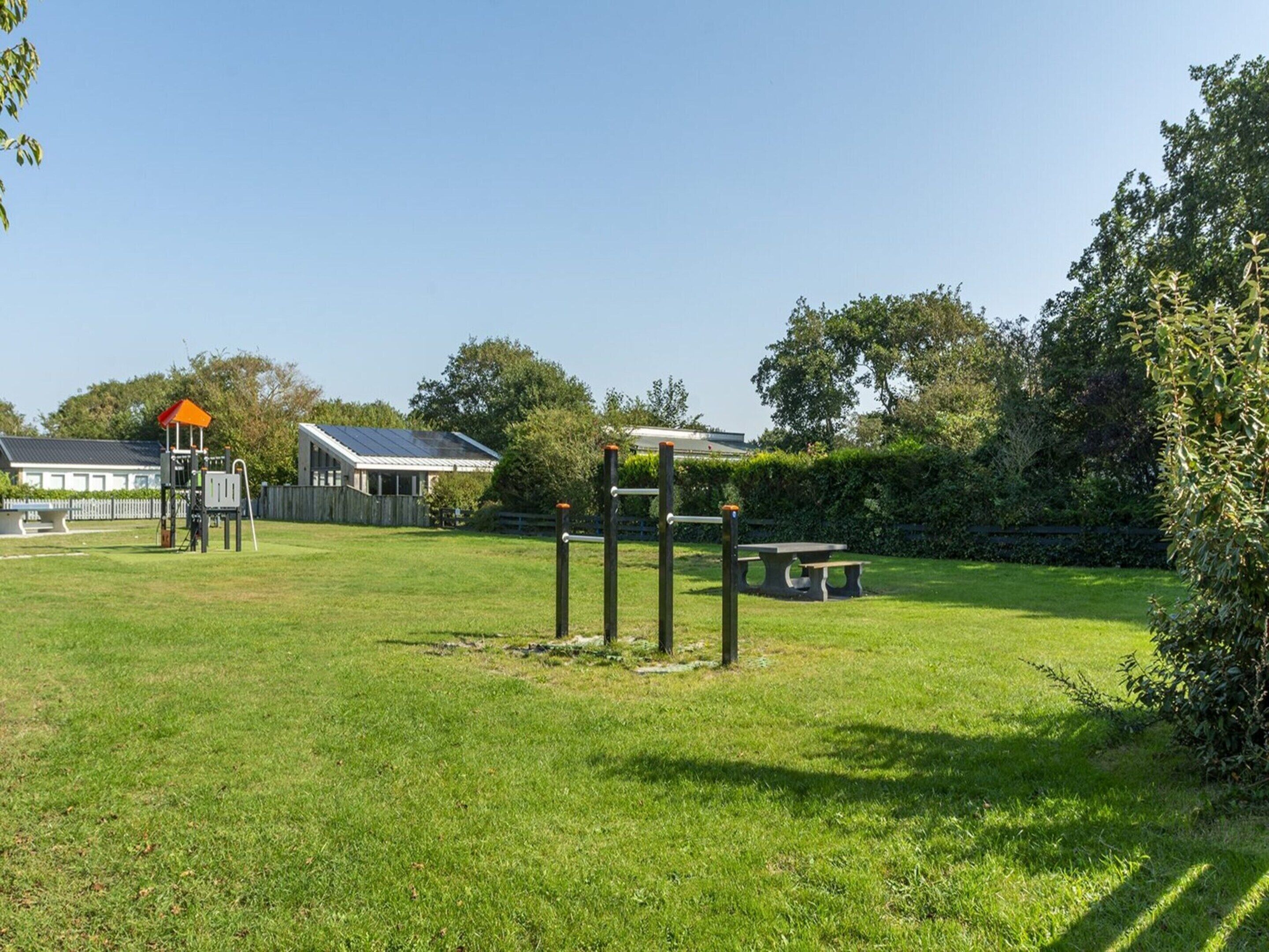 Un espacio al aire libre con césped, un parque infantil, una mesa de picnic y un edificio con techo inclinado.