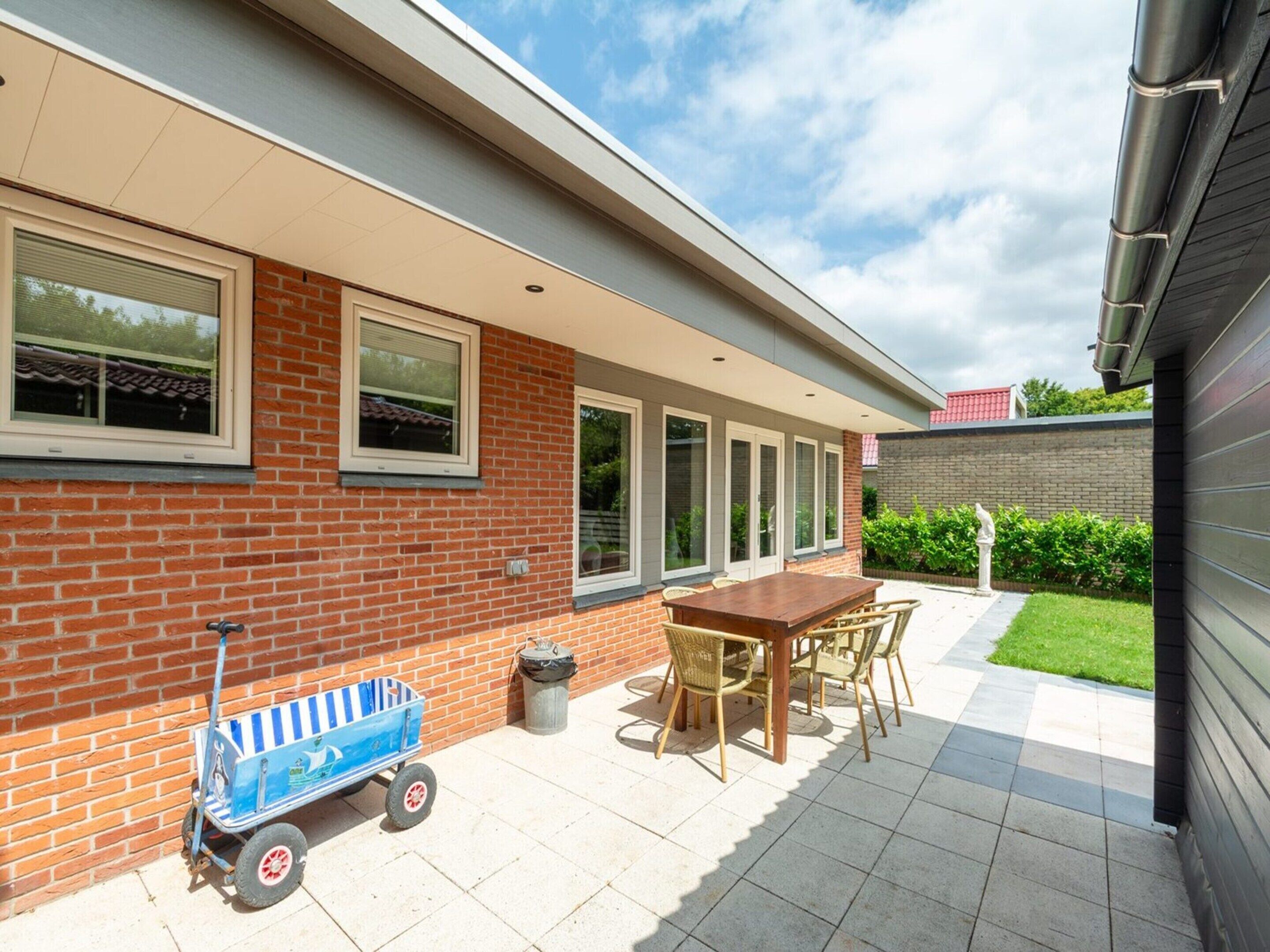 A patio with a table and chairs, a small blue cart, and a trash can.