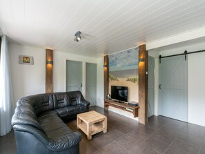 A living room with a sectional sofa, a coffee table, a flat-screen TV, and a large painting of a beach scene. - Bungalow Near Dutch Coast With Private Garden (Callantsoog)