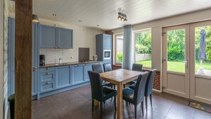 Une cuisine moderne avec des meubles bleus, une table à manger en bois et une vue sur le jardin grâce à de grandes portes-fenêtres coulissantes.