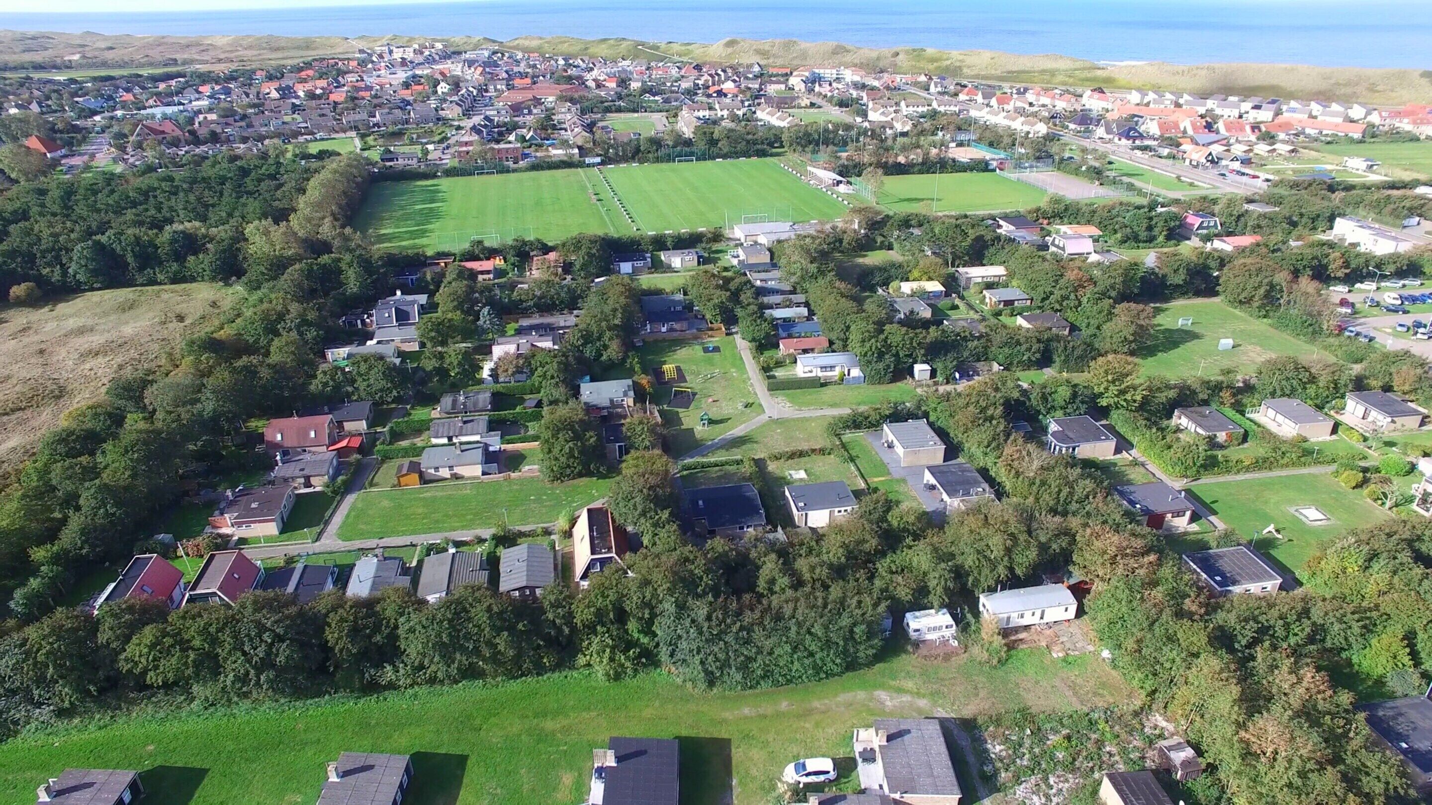 An aerial view of a residential area with houses, green spaces, and a large open field.
