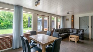 Un vaste espace de vie comprenant une table à manger en bois, un canapé en cuir et de grandes fenêtres donnant sur l’extérieur.