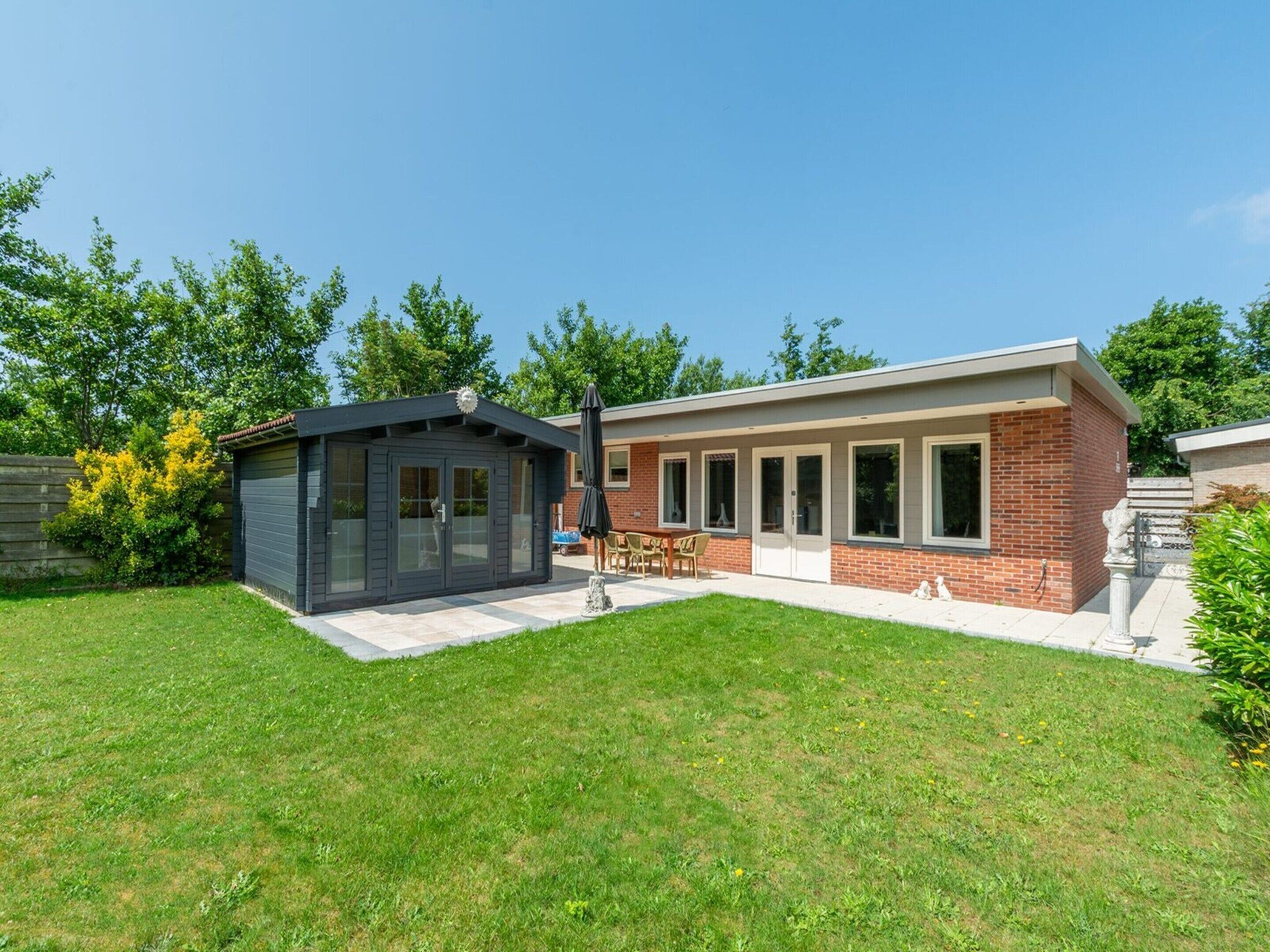 Une maison moderne avec un garage, une terrasse dotée d’une table et de chaises, et une pelouse bien entretenue.
