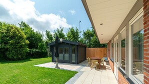 Une maison moderne dotée d’un patio, d’un petit abri de jardin et d’une cour arrière clôturée.