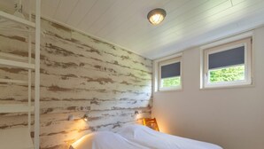 Une chambre à coucher avec un lit, deux fenêtres, un mur en bois et un luminaire au plafond.