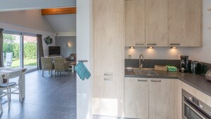 Et moderne køkken med lyse træskabe, en indbygget ovn og et spiseområde med et bord og stole.