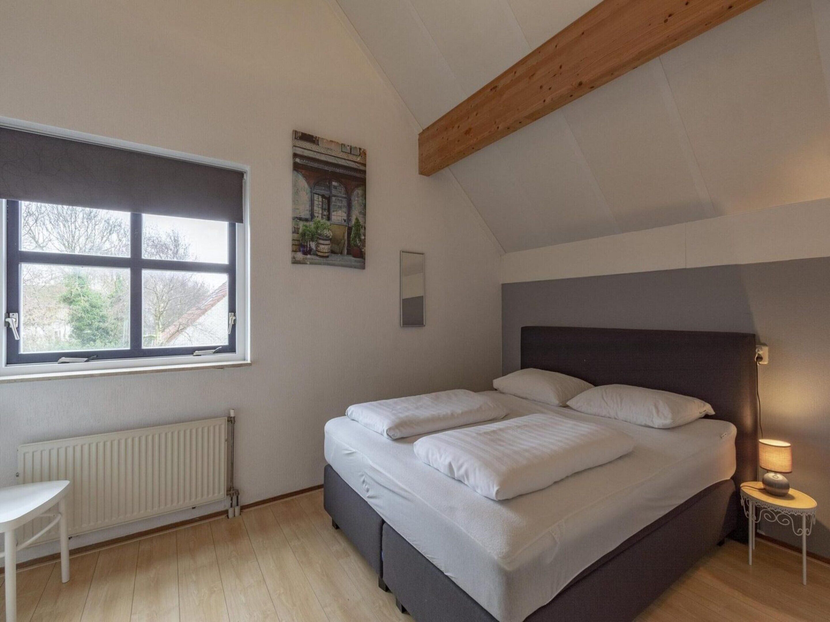 Une chambre à coucher avec un grand lit, une fenêtre, un radiateur et une petite table de chevet avec une lampe.