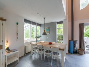 Uma cozinha moderna com mesa de madeira, cadeiras brancas, fogão e janelas amplas.