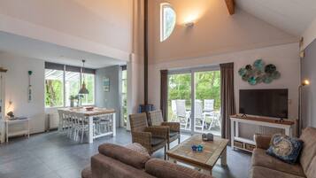 A spacious living area with a sofa, coffee table, and TV. There is a dining area with chairs and a table, and a large window providing natural light.