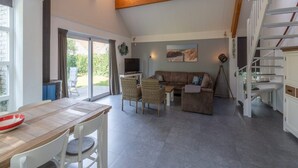 En rummelig opholdsstue med træloft, et spisebord og en sofa.